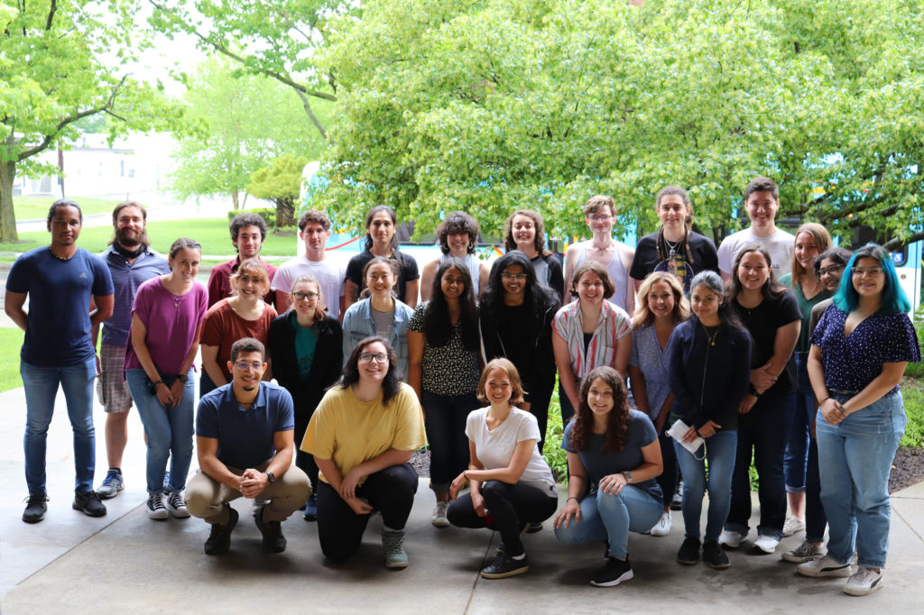 A group photo of 27 undergraduate interns outside of BTI, with trees in the background.