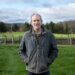 Boyce Thompson Institute researcher standing outdoors on a farm in front of green fields and livestock, emphasizing agricultural research and plant science.