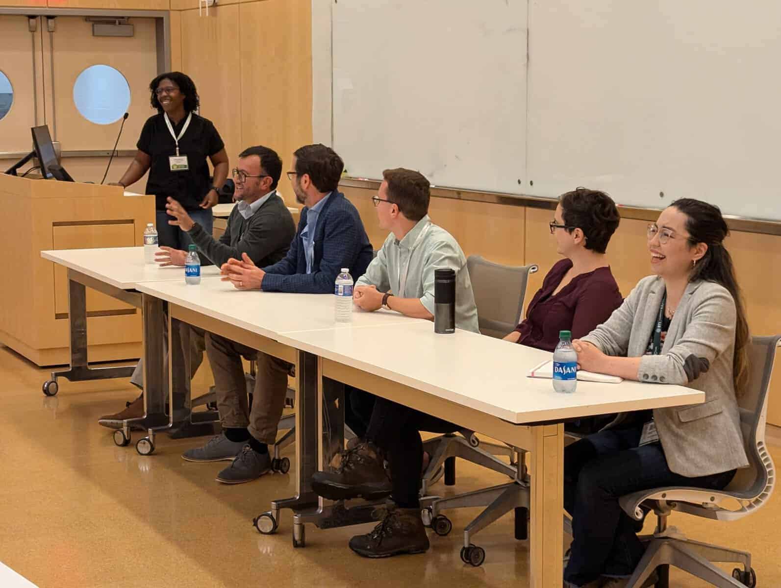 A group of mentors sitting at a table, talking, while the moderator looks on in the background