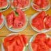 Watermelon slices on white plates arranged on a wooden table, showcasing fresh, juicy fruit perfect for summer snacks. Ideal for healthy eating, fruit displays, and refreshment options.