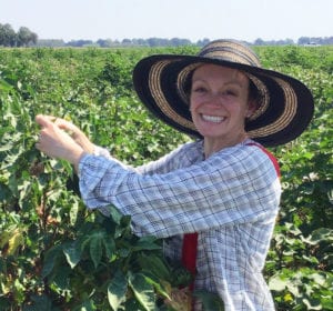 A medium shot of Michelle Heck in a field of crops, smiling and wearing a sun hat.