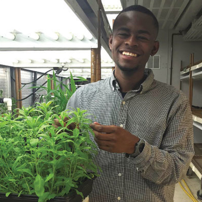 Brandon Williams stands with a plant in a growth chamber