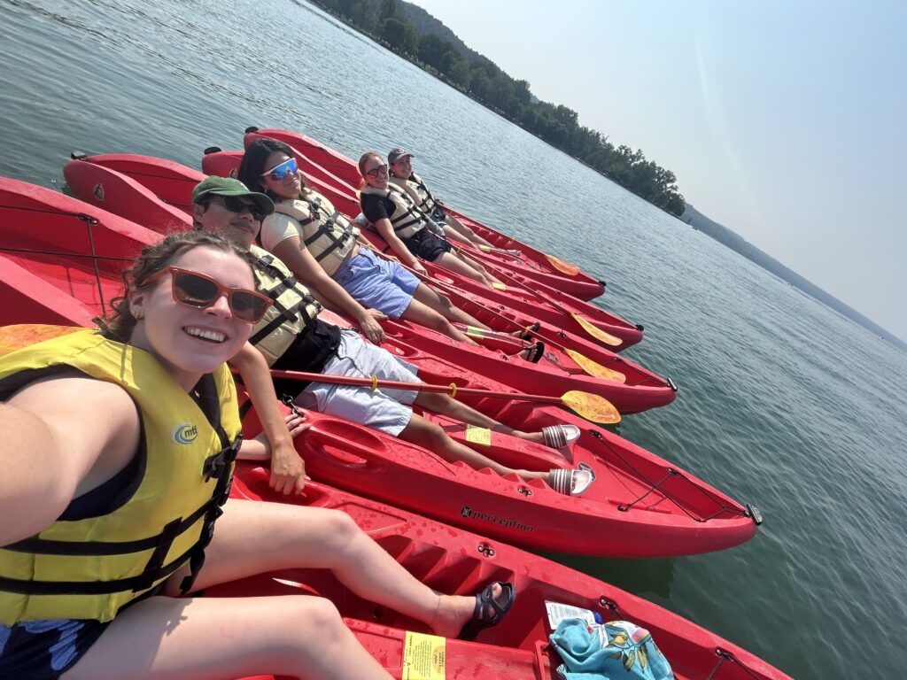 Kayaking group A group of five people in red kayaks wearing life vests, smiling and relaxing together on a sunny lake.