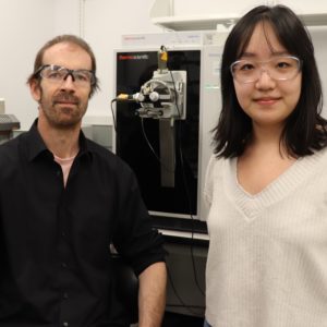 Frank Schroeder and Jingfang Yu pose on either side of a mass spec machine.