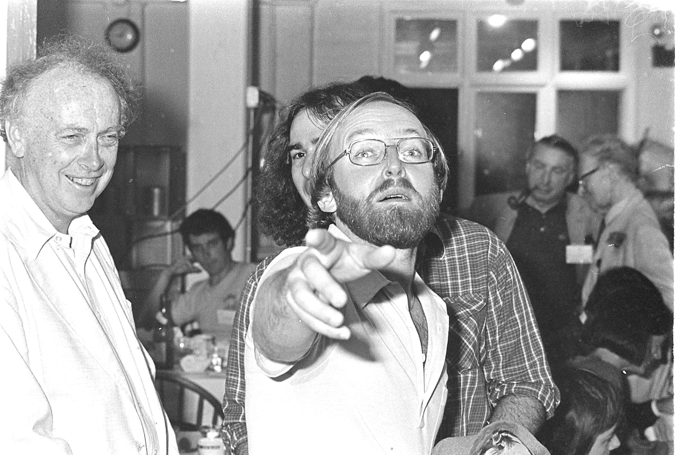 A black and white photo of Dan Klessig points at the camera, with James Watson smiling behind him.